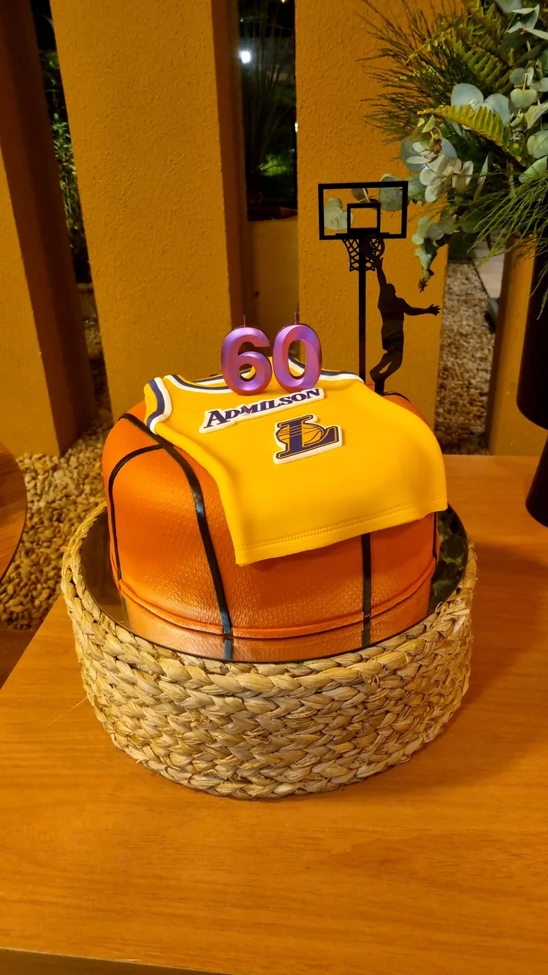 Bolo de aniversário em forma de bola de basquete coberta por uma camisa amarela, com o número 60 no topo.