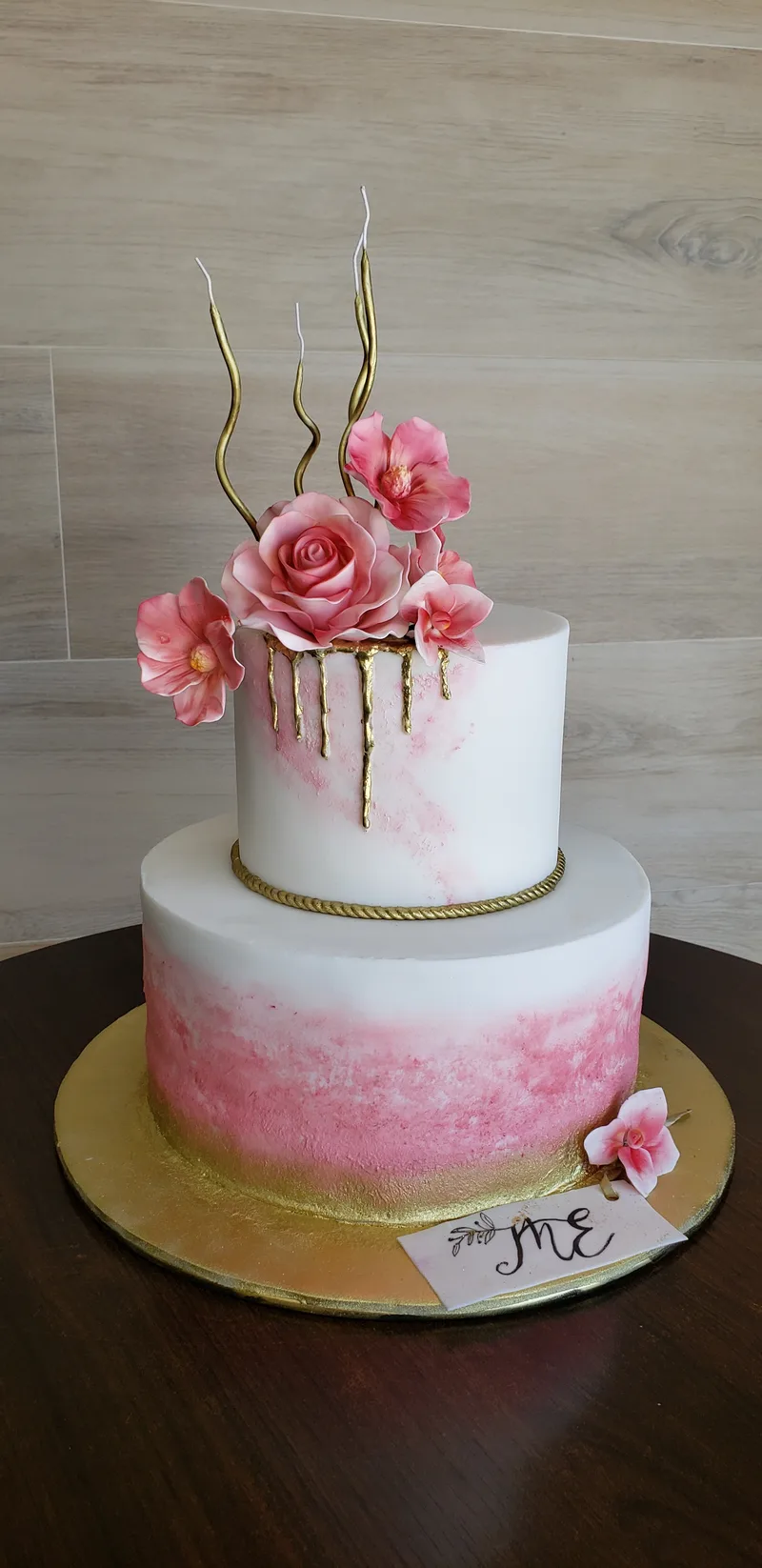Bolo de aniversário de dois andares com degradê aquarela rosa, rosas de pasta e hastes douradas no topo.