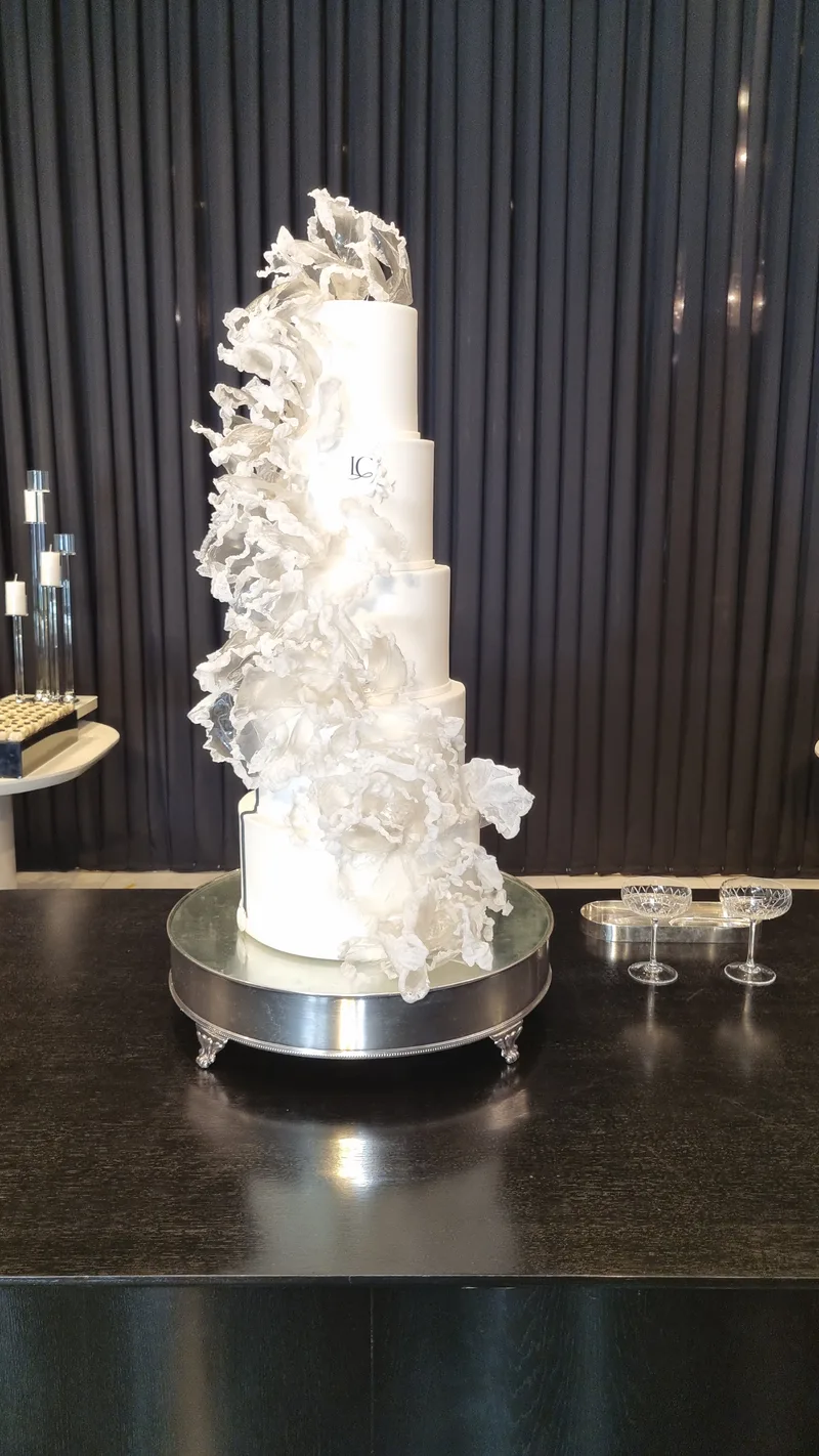 Bolo de casamento alto e branco, com ondas de pasta caindo em cascata por uma das laterais.