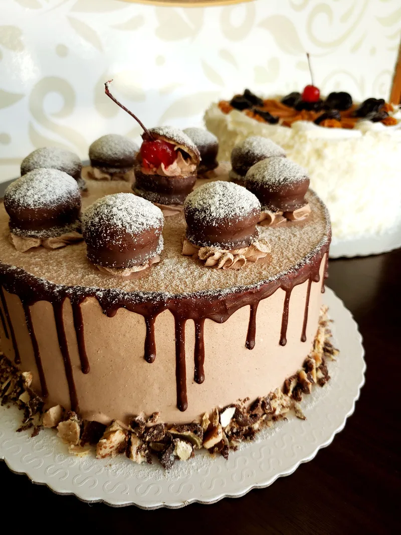 Bolo cremoso de chocolate com cobertura escorrendo e doces redondos com cereja no topo.