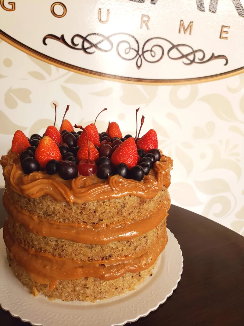 Bolo naked com camadas de doce de leite e topo de frutas vermelhas e cerejas.