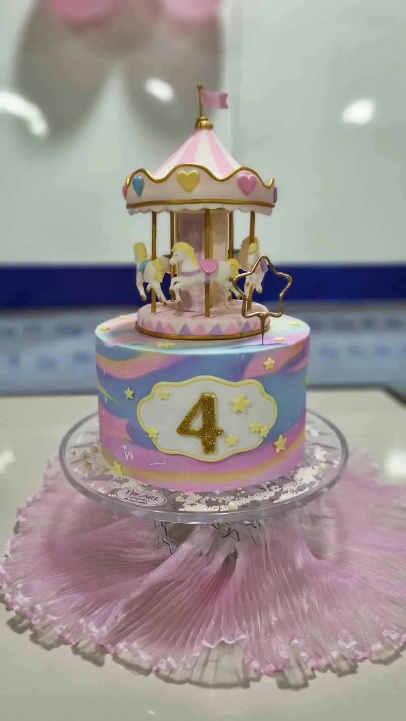 Bolo infantil marmorizado em rosa, azul e lilás, com um carrossel de biscuit no topo e o número 4.